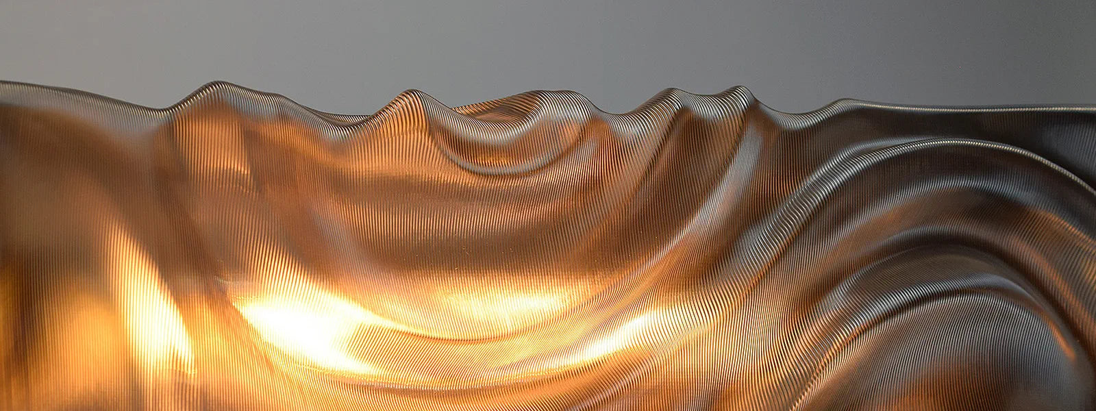 Metallic, wavy surface with a warm glow on a gray background