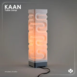 White matte textured table lamp with 'KAAN' branding on a gray background with the light turned on. Created by MODEO Design